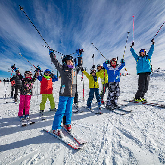 Jubilant group of children and their instructor holding skiis in the air on Mt Hotham